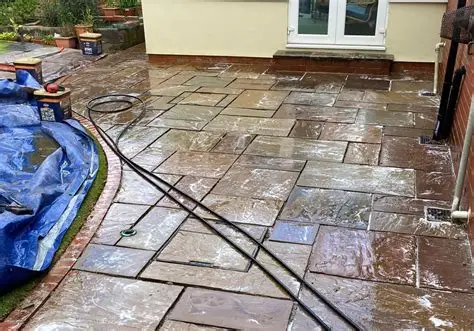 Freshly installed Indian sandstone patio slabs showing a rich, polished wet finish near a garden doorway.